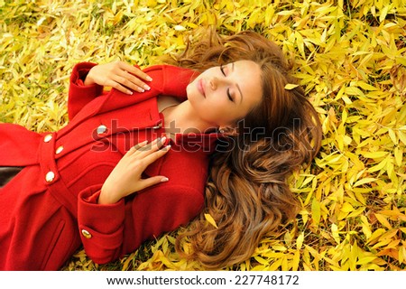 Attractive young woman in red coat lying in autumn leaves, outdoor.