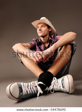 young smiling guy in sneakers and hat sitting against brown background