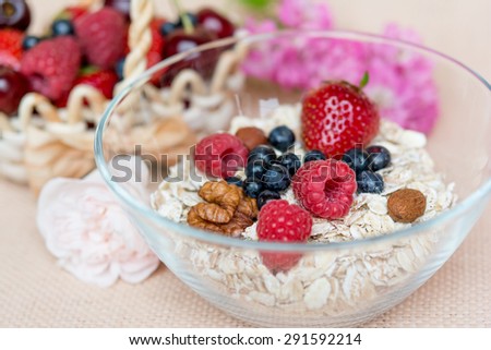 A bowl with hole grain flakes, berries, nuts and rose on sackcloth, beige background. Healthy breakfast