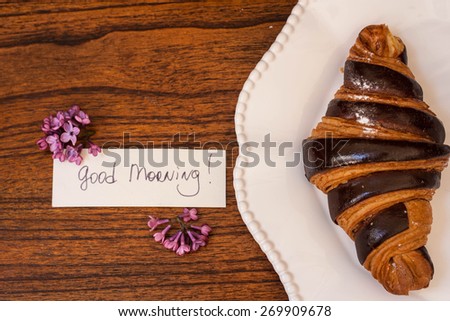 Croissant on the plate with lilac and good morning note