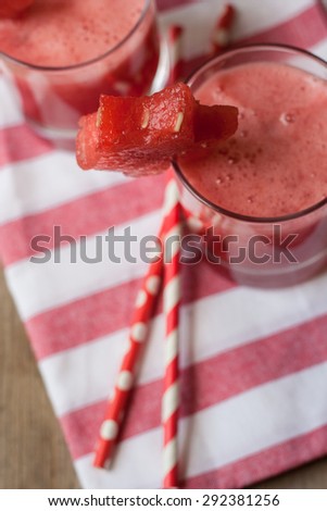 Watermelon smoothie on a red striped napkin and two straws on a wooden background