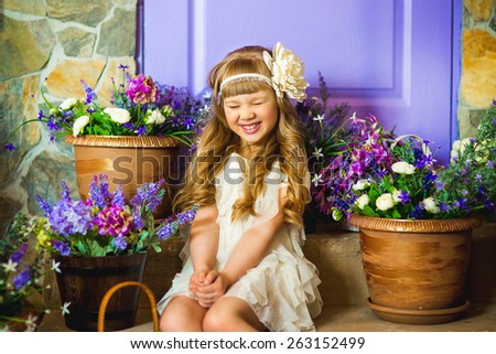 the girl in a cream dress sits on a ladder near pots with lilac flowers