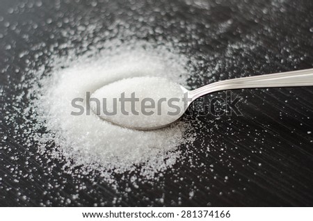 white sugar scattered on a metal spoon on a black table