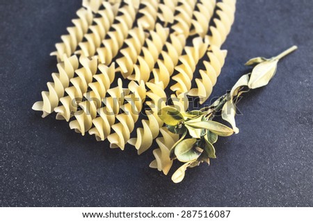 Retro food background: Spiral pasta on a dark cloth background with a sprig of herbs. Top view