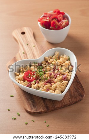A heart shaped plate of scrambled eggs garnished with cress, chives and cherry tomato.