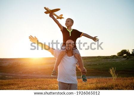 Dad holds his son around his neck at sunset in the summer they launch a plane against the background of the sky