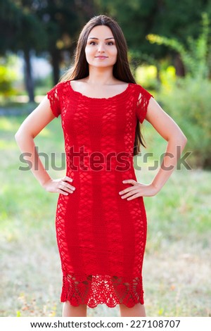 Beautiful young caucasian woman posing in a red handmade knitted dress outdoors