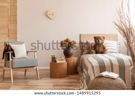 Flowers in brown vase on wooden nightstand table next to single bed with stripped bedding with teddy bear