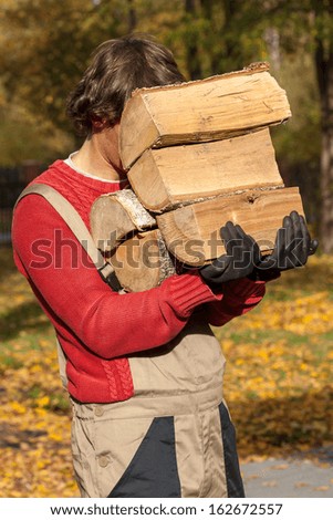 Young worker holding a stack of firewood during his part-time job.