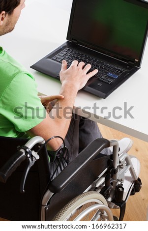 Young employee on wheelchair during work on computer
