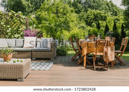 Dining table covered with orange tablecloth standing on wooden terrace in green garden
