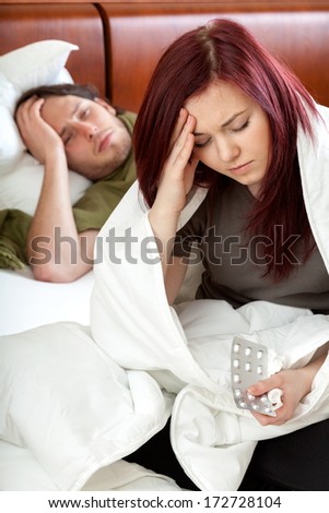 Husband and wife suffering headache, woman taking pills
