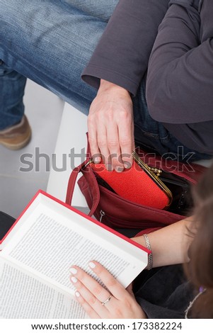 A thief taking a purse out of a woman\'s reading a book bag