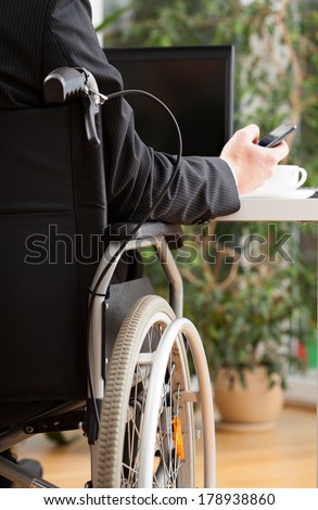 Businessman on wheelchair texting during his work in office