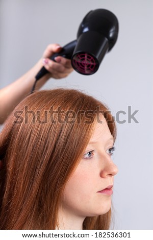 Professional hairdresser styling girl\'s hair by hair dryer