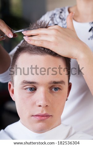Professional hairdresser cutting young man\'s hair in beauty studio