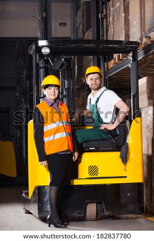 Female worker in vest and male worker in forklift at warehouse