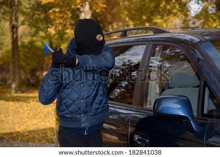 A masked man robbing a car by breaking the window