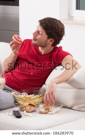 Young male couch potato eating donuts