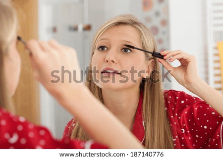 A pretty blonde woman applying black mascara on her lashes