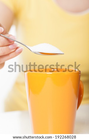 Woman in yellow t-shirt sweetening tea or coffee