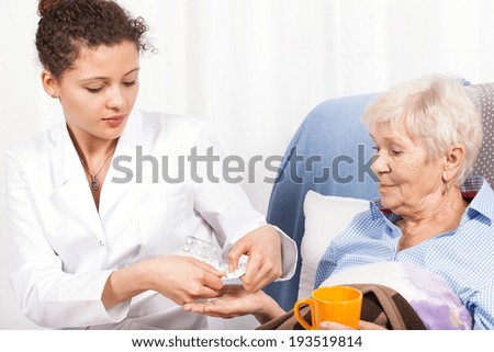 Home nurse giving elderly woman vitamin pills