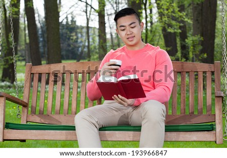 Asian man reading book in a garden