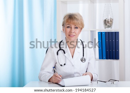 Female doctor in laboratory coat with stethoscope making notes