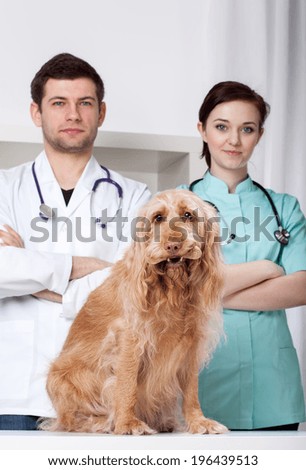 Two veterinarians standing behind dog with bone