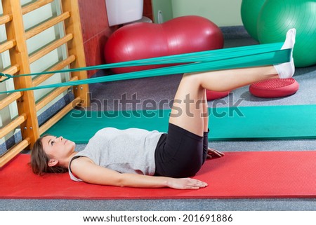 Girl lying on exercise mat and stretching legs with elastic band