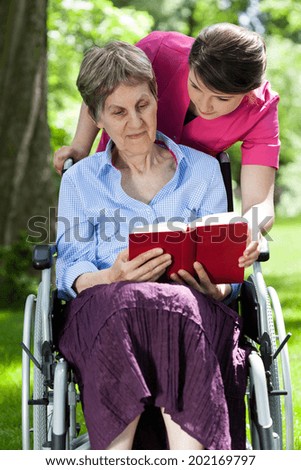 Woman on wheelchair reading book in a garden