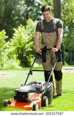 Man in work overalls mowing lawn, vertical