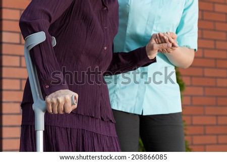 Lady on crutches and nurse in uniform outside the house