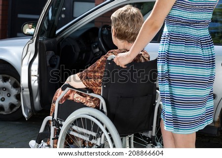 A young woman is carrying an old lady in a wheelchair to the car