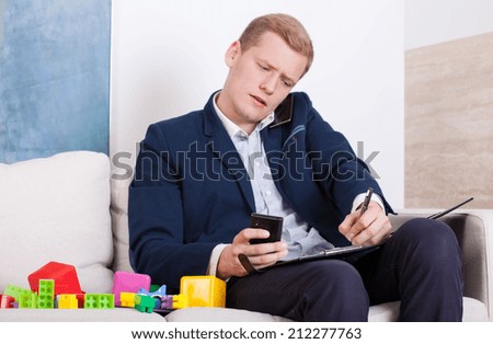 The busy man sitting on the couch with the phone and taking notes