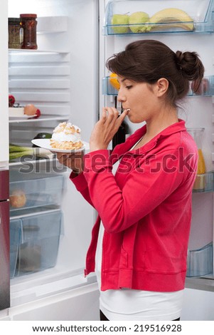 Girl eating cream cake near the refrigerator