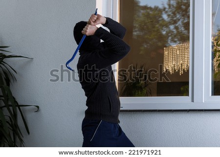 Burglar with obscured face trying to break the window