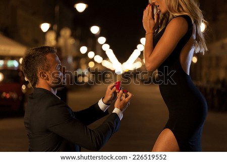 A man in a suit proposing to his beautiful woman at night