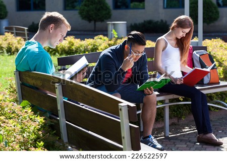 Young people sitting on the bench and studying to the exam