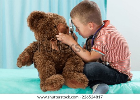 Little boy playing on doctor and examining teddy bear