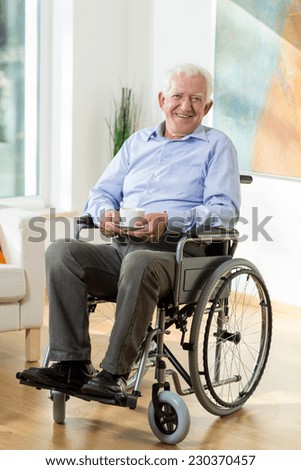 Older smiling man on wheelchair with cup of hot coffee
