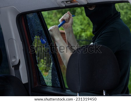 Burglar with crowbar breaking car window, horizontal