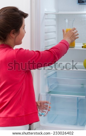 Young pretty woman reaching for orange juice in the fridge