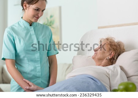 Young pretty nurse and her older sick patient in hospital bed