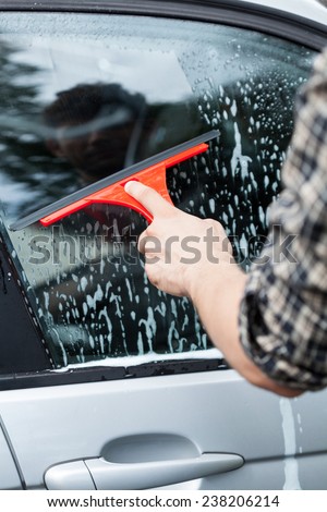 Close-up of man\'s hand cleaning the car window by squeegee