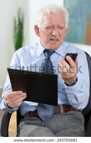 Elderly businessman having problems with using phone