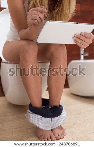 Young woman sitting on water closet and checking her tablet