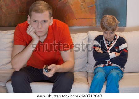 Immature dad watching tv and his bored son