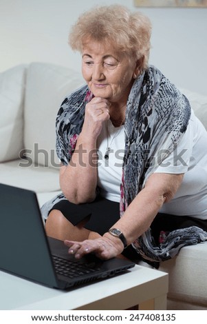 Elderly woman sitting on sofa and using laptop