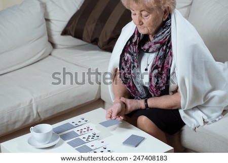 Senior woman sitting on the couch and playing cards alone